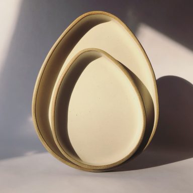 Two nested tear-shaped stoneware plates with a cream satin glaze